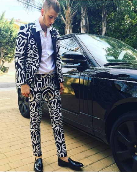 MIllionaire musician, Machine gun kelly wearing black & white suit and driving expensive thousand dollar car. He is living a lavish lifestyle in rich manner.